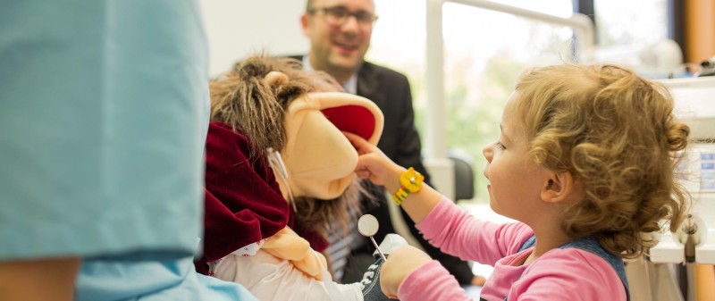 Kind spielt mit Handpuppe im Zahnarztstuhl zur Beruhigung.